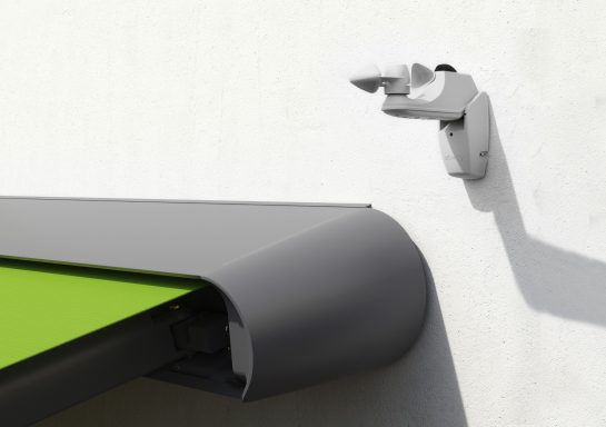 Sonnen- und Windsensor an der Wand neben einer grünen Markise.