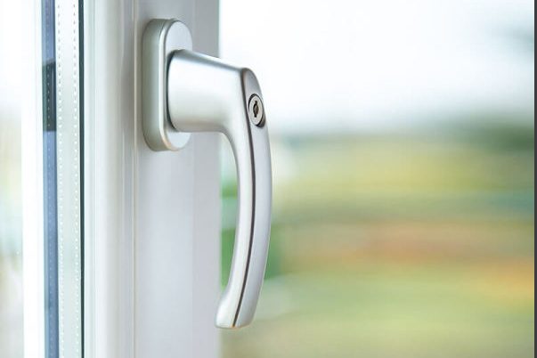 Silberner Fenstergriff an einer verglasten Tür mit unscharfem Hintergrund.