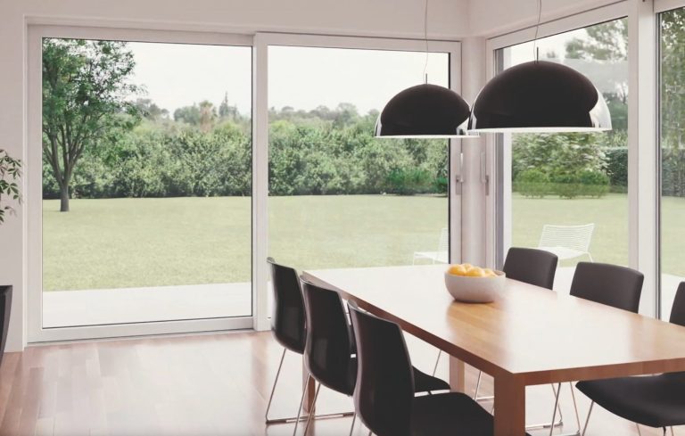 Moderne Esszimmer mit einem Holztisch, schwarzen Stühlen und großen Fenstern zum Garten.