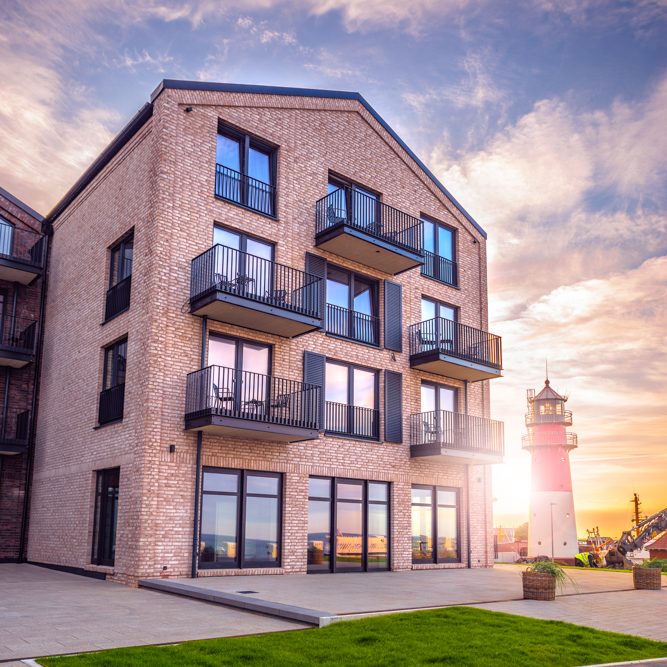 Moderne Wohnung mit Balkon, Leuchtturm im Hintergrund und sunset Farbenspiel.