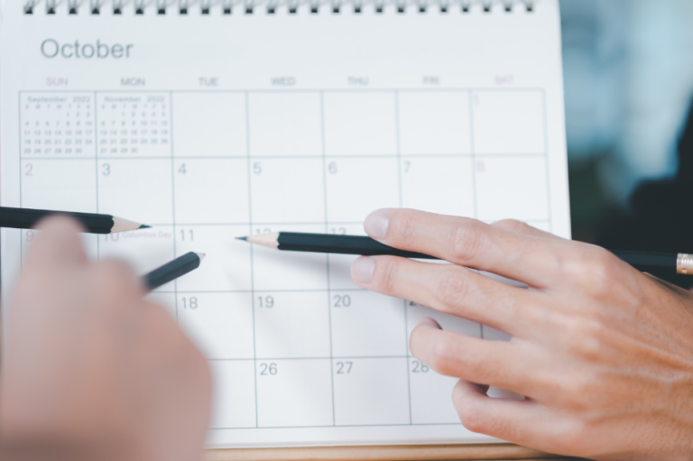 Hände, die einen Kalender für Oktober mit Stiften markieren.