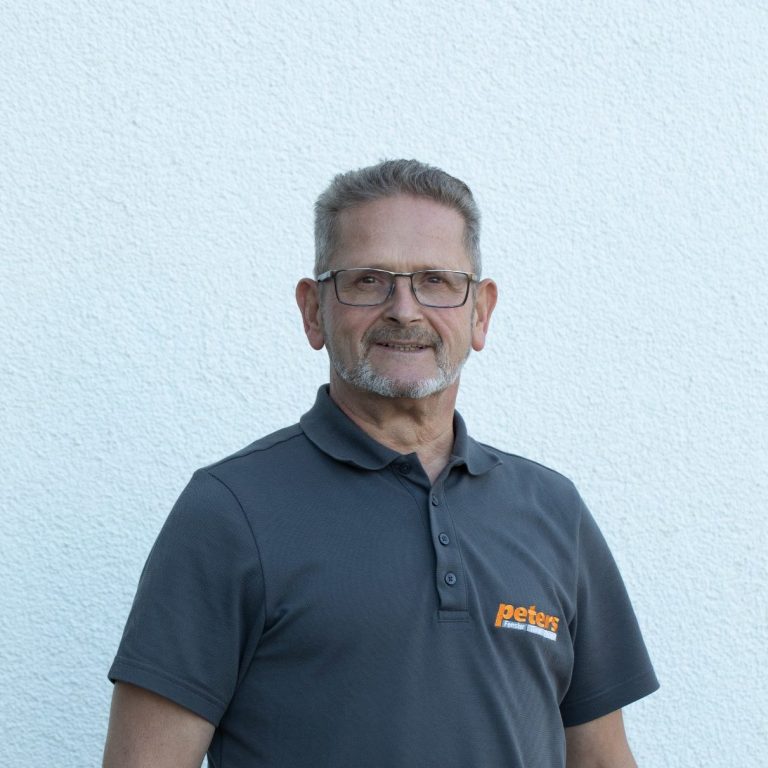 Lächelnder Mann in grauem Poloshirt vor hellem Hintergrund.
