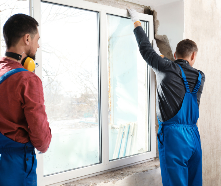 Zwei Handwerker montieren ein Fenster in einem Raum mit Renovierungsarbeiten.