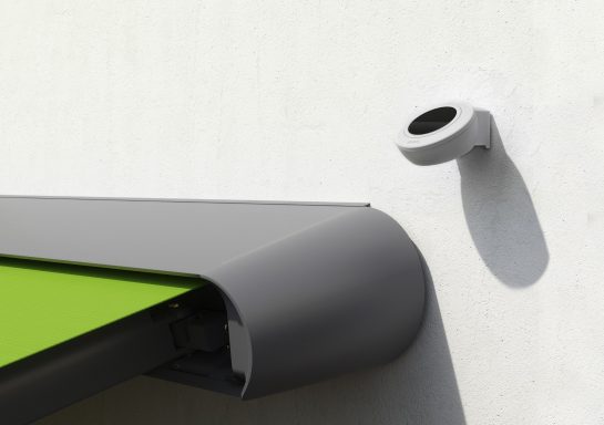 Eine graue Dachrinne mit einer weißen Regensensor an einer Wand.