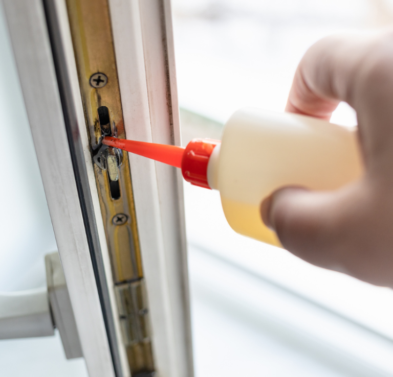Eine Hand hält eine Flasche mit Flüssigkeit, die in einen Fensterbeschlag getropft wird.