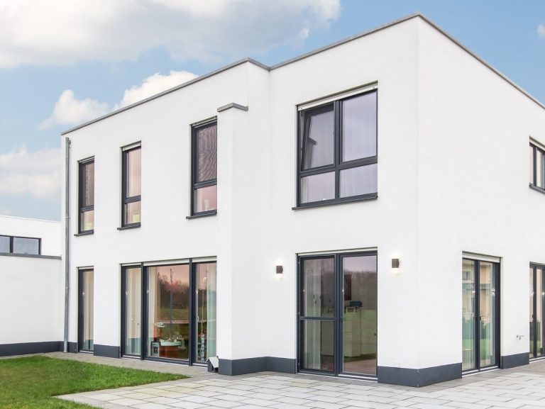Modernes, zweigeschossiges, weißes Wohnhaus mit großen Fenstern und flachem Dach.