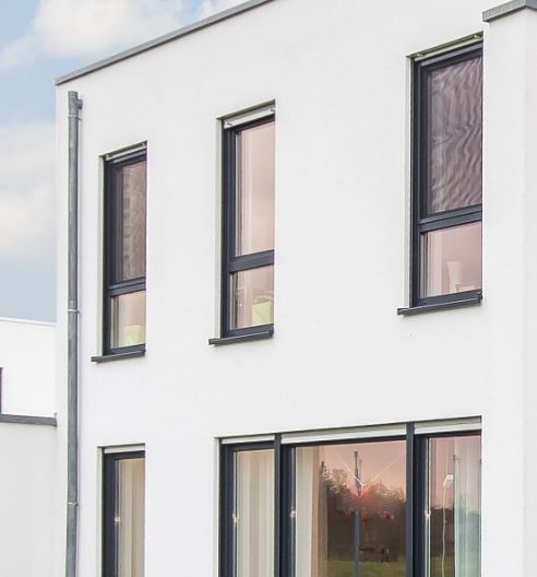 Modernes zweigeschossiges Gebäude mit weißen Wänden und großen Fenstern.